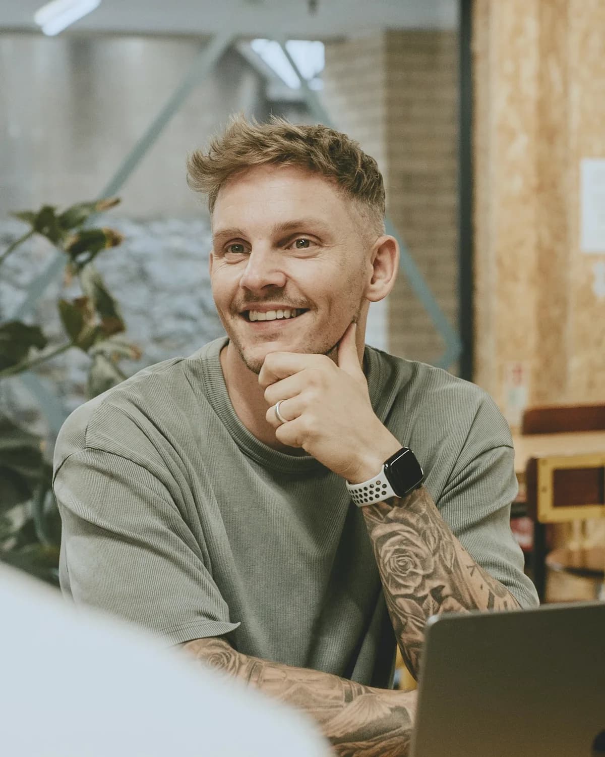 Homem sorrindo, sentado diante do notebook numa conversa de trabalho